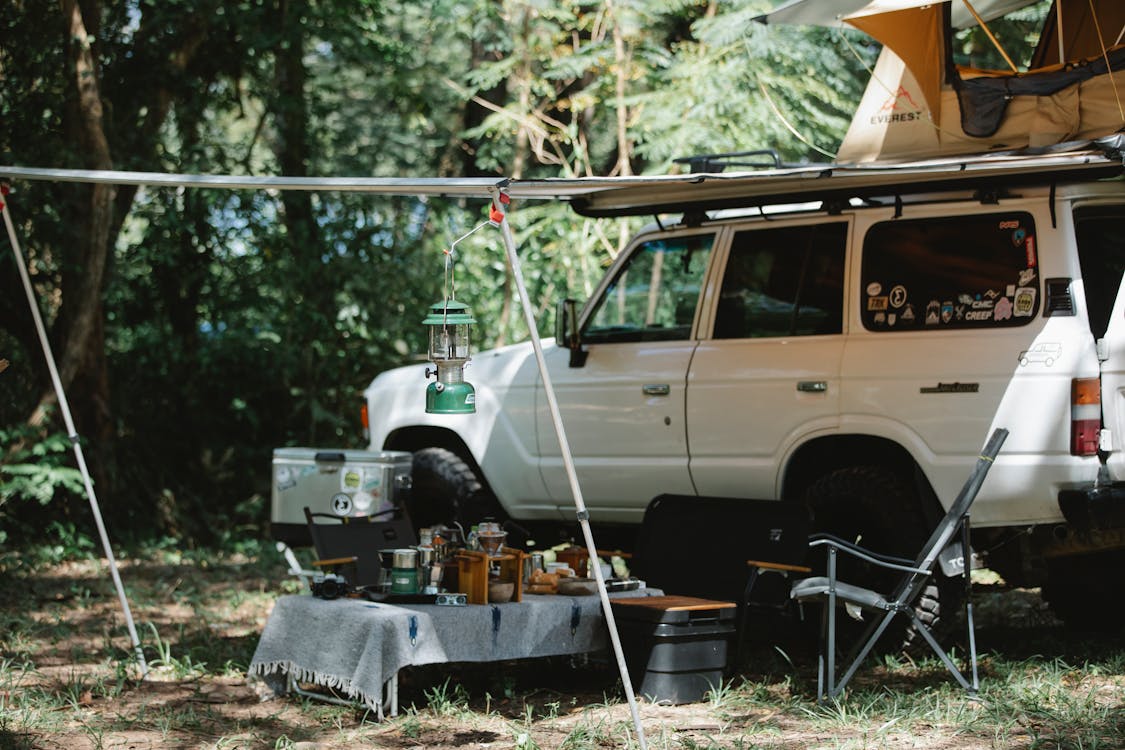 Free Camper offroader with roof top tent and awning camping in nature among green trees in sunny day Stock Photo