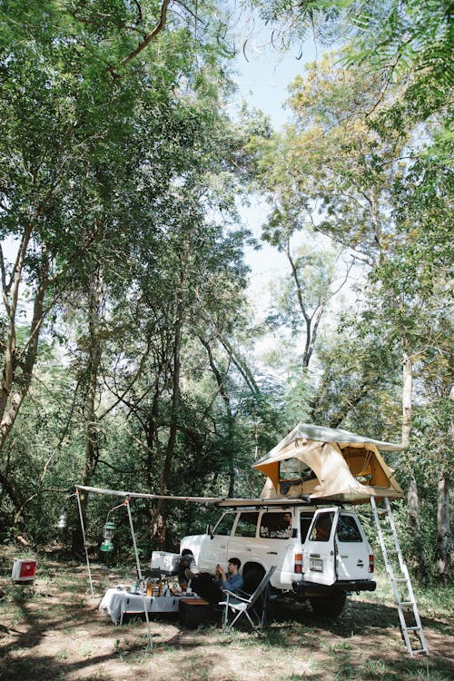 Camping car with tent on roof parked in forest in sunlight