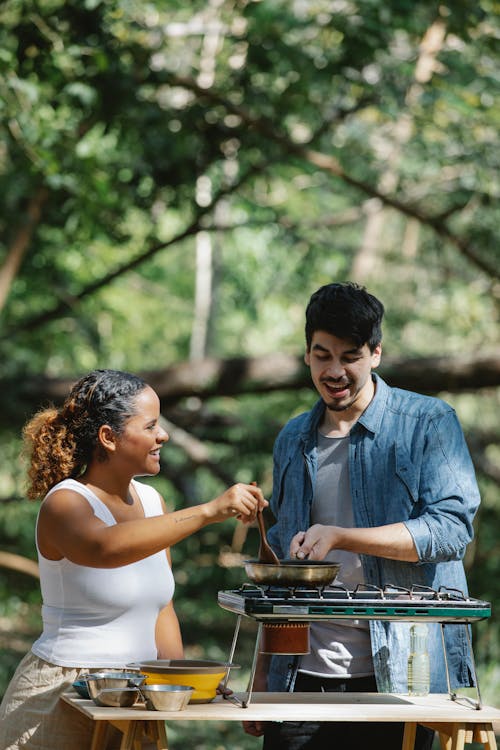 Cheerful multiracial couple cooking on stove in forest