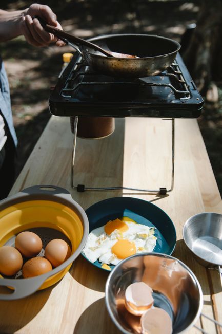 A cast iron skillet with vegetables and tortillas cooking on a compact camp stove at a campsite