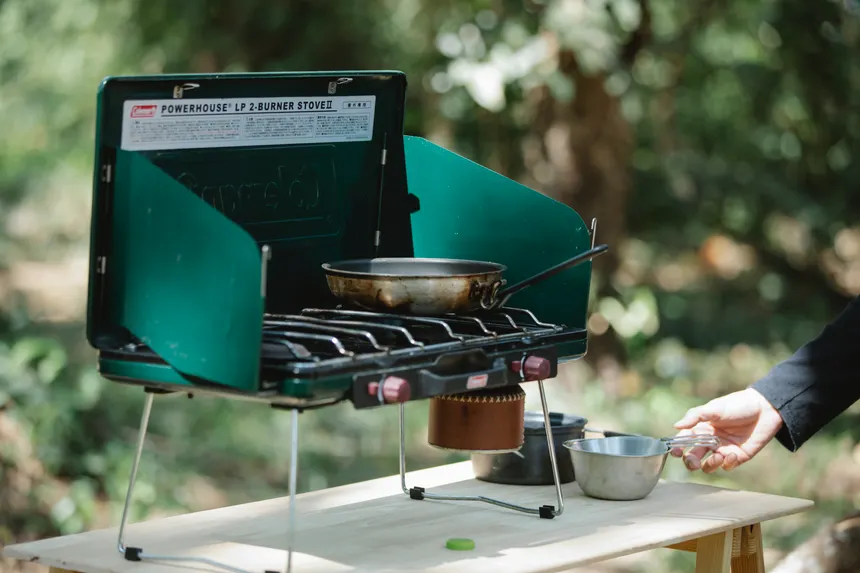 Crop unrecognizable male cooking on modern metal burner stove using skillet in forest