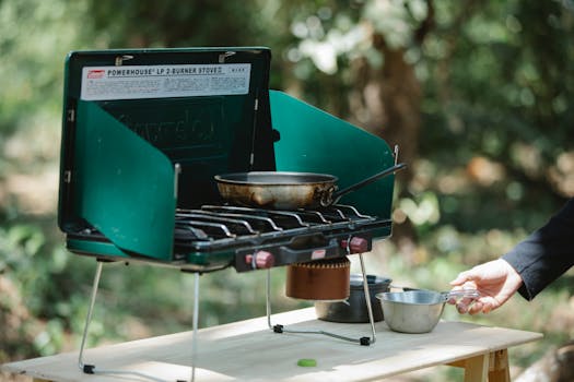 A portable gas stove with pan and equipment outdoors, perfect for camping cooking.