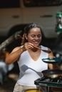Happy young Hispanic female cook putting eggs on plate fried on pan on metal gas burner in camp against blurred car