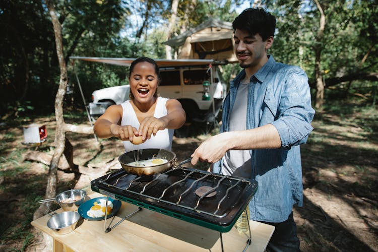 Cheerful Diverse Couple Frying Eggs On Gas Burner