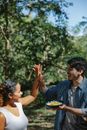 Cheerful young multiracial couple in casual outfits with plate of scrambled eggs in forest giving each other high five
