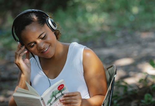 Smiling ethnic woman reading book in headphones