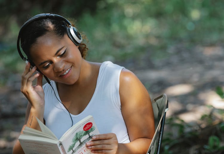 Smiling Ethnic Woman Reading Book In Headphones