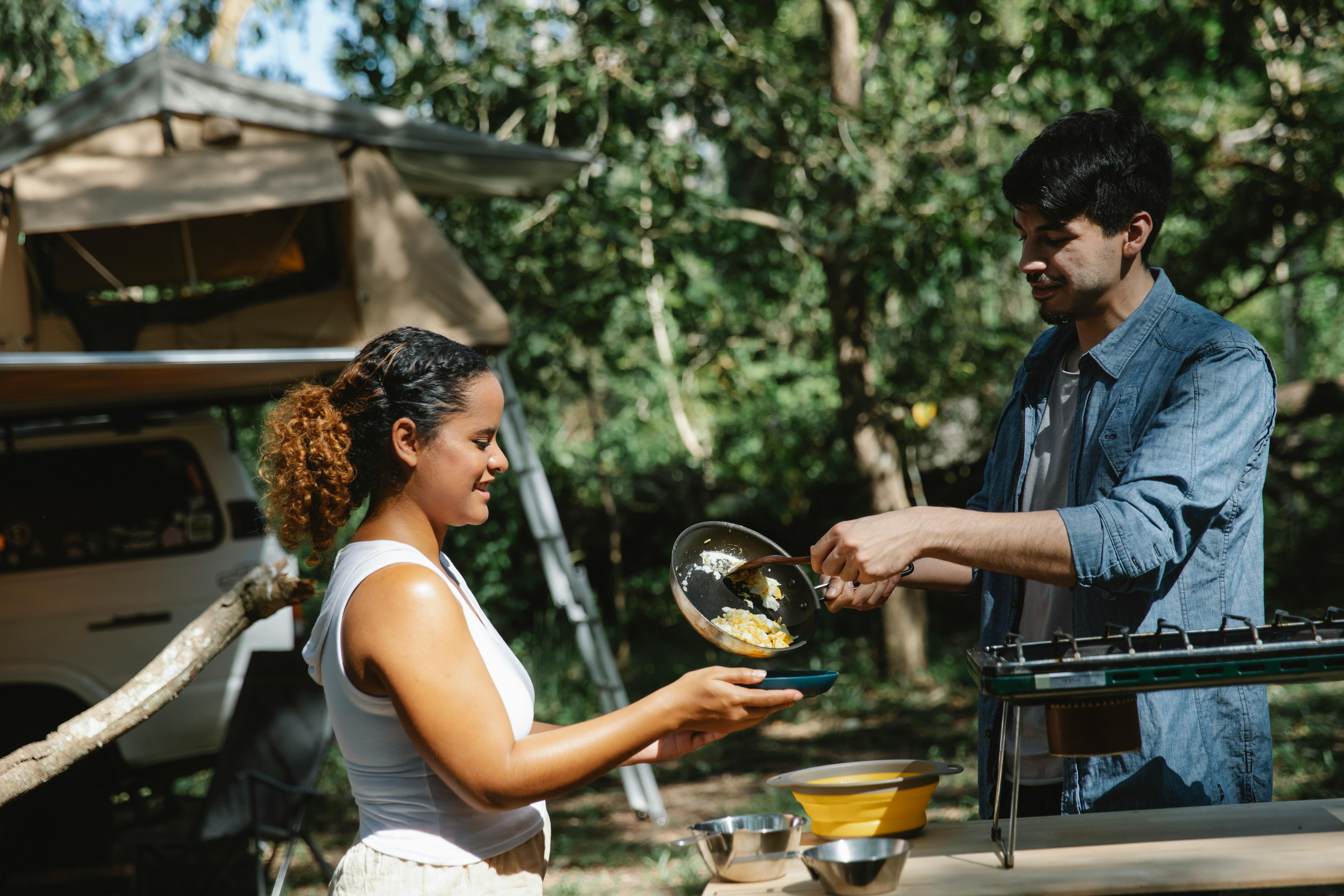 happy couple putting scrambled eggs on plate in camp