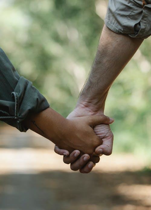 Crop couple holding hands walking in park