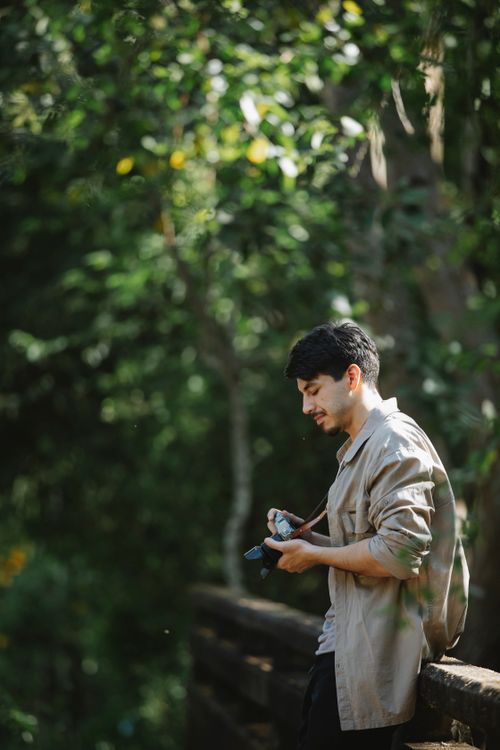 Free Side view of glad young bearded male photographer with retro camera standing near wooden fence of footbridge in park Stock Photo