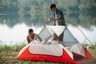 Concentrated young multiethnic couple putting up bright colorful tent on bank of river covered with grass