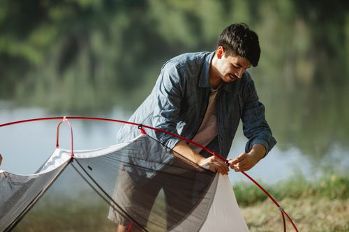 Free Focused young male tourist in casual outfit standing on river bank and putting up tent in summer day Stock Photo