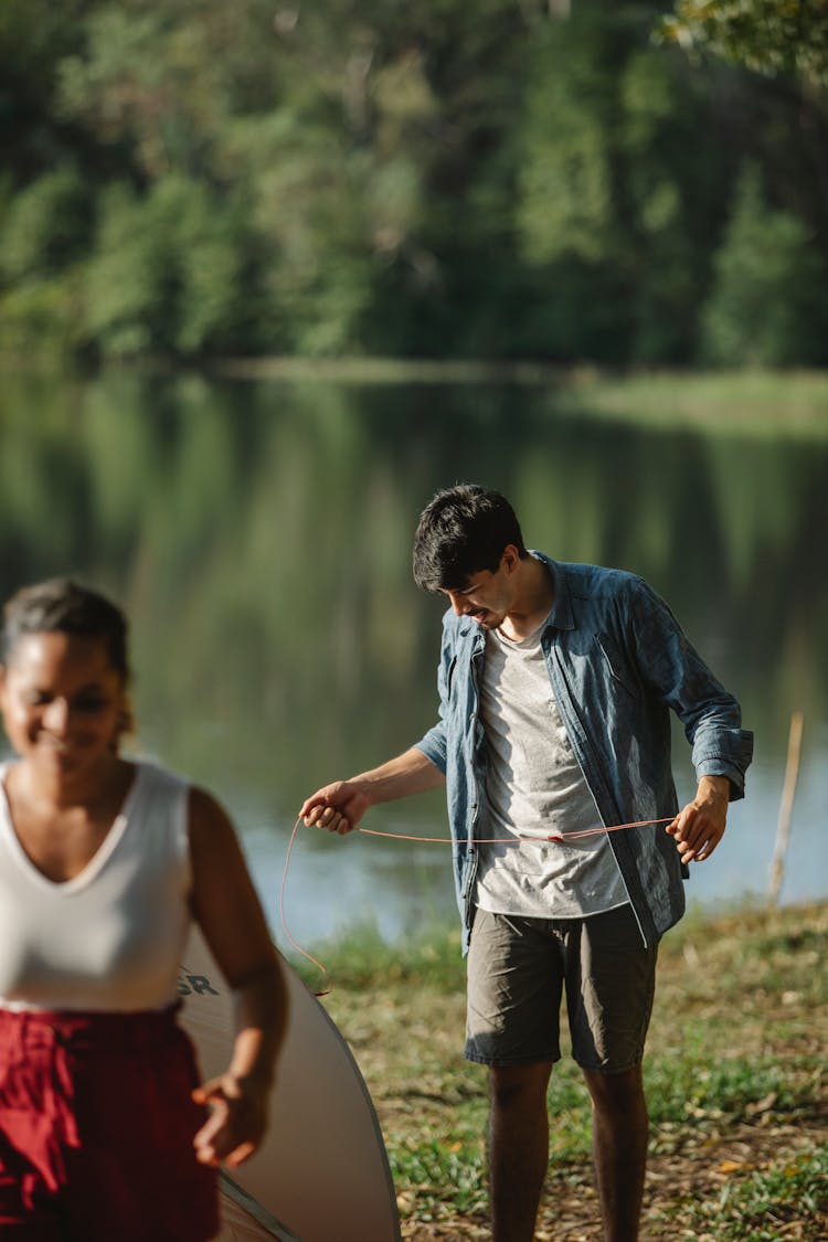 Diverse Couple Of Tourists With Tent On River Bank