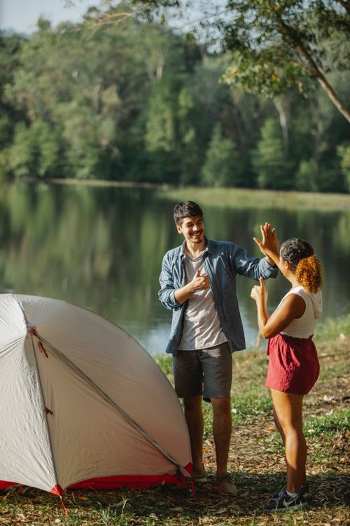 Free Content male tourist and anonymous ethnic female beloved giving high five with thumbs up while looking at each other on river coast Stock Photo