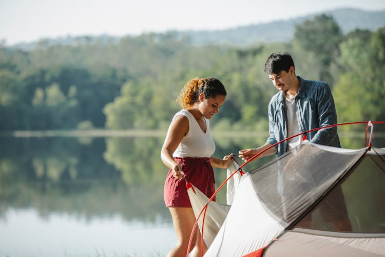 Multiracial Couple Of Tourists Setting Up Tent Against River