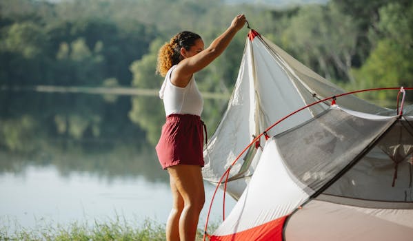 A woman sets up a tent by a serene lakeside, enjoying a sunny day outdoors.