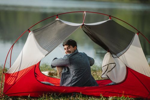 Free Back view of content tourist resting in tent on lake coast while looking at camera over shoulder Stock Photo