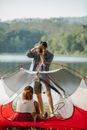 Smiling male traveler taking photo of anonymous ethnic female beloved in tent on camera against lake