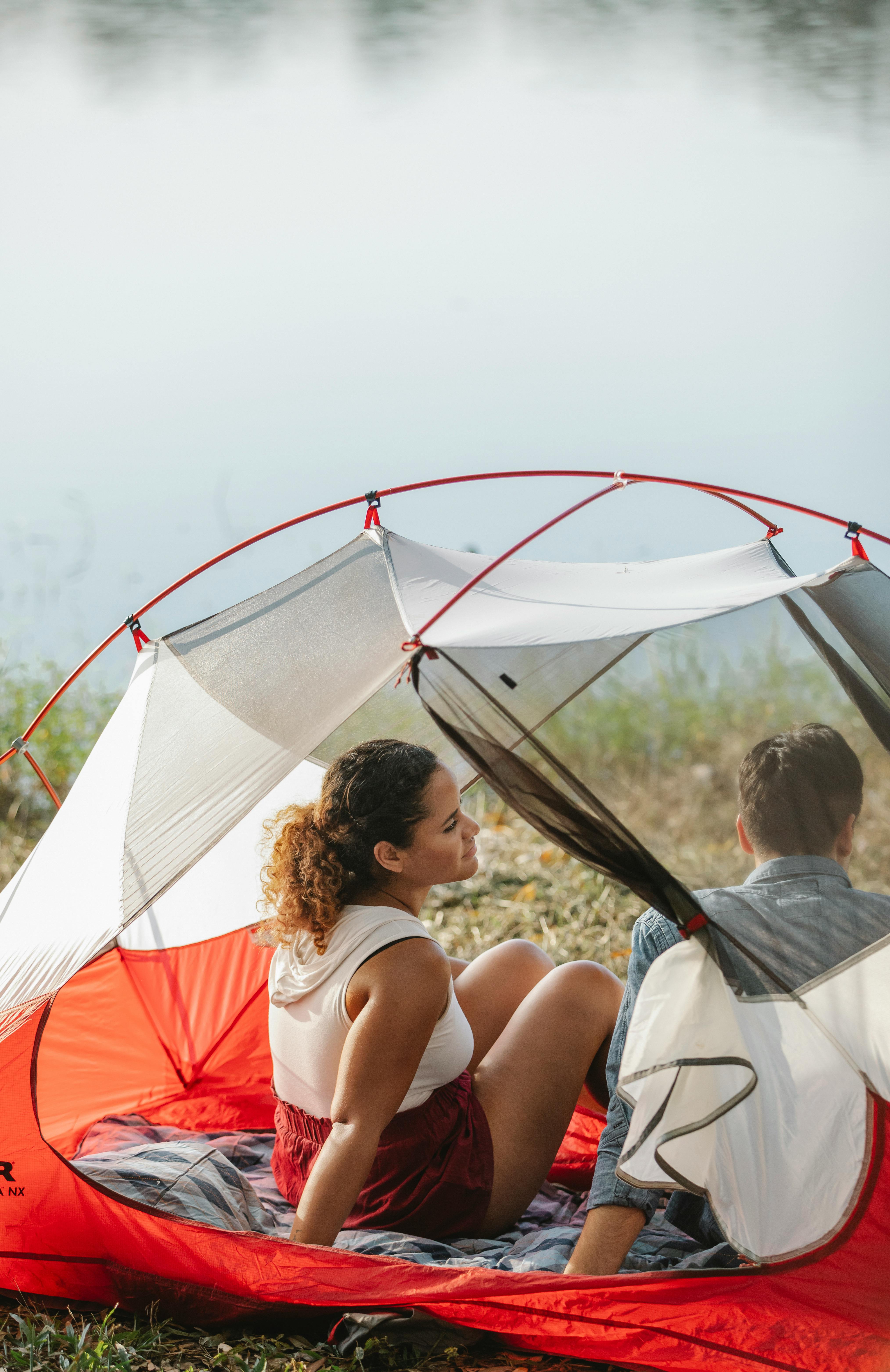 diverse couple of hikers interacting in tent against river
