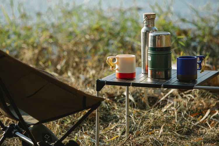 Thermoses And Mugs On Camping Table On Coast