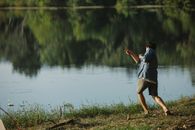 Unrecognizable traveler throwing stone into lake from shore