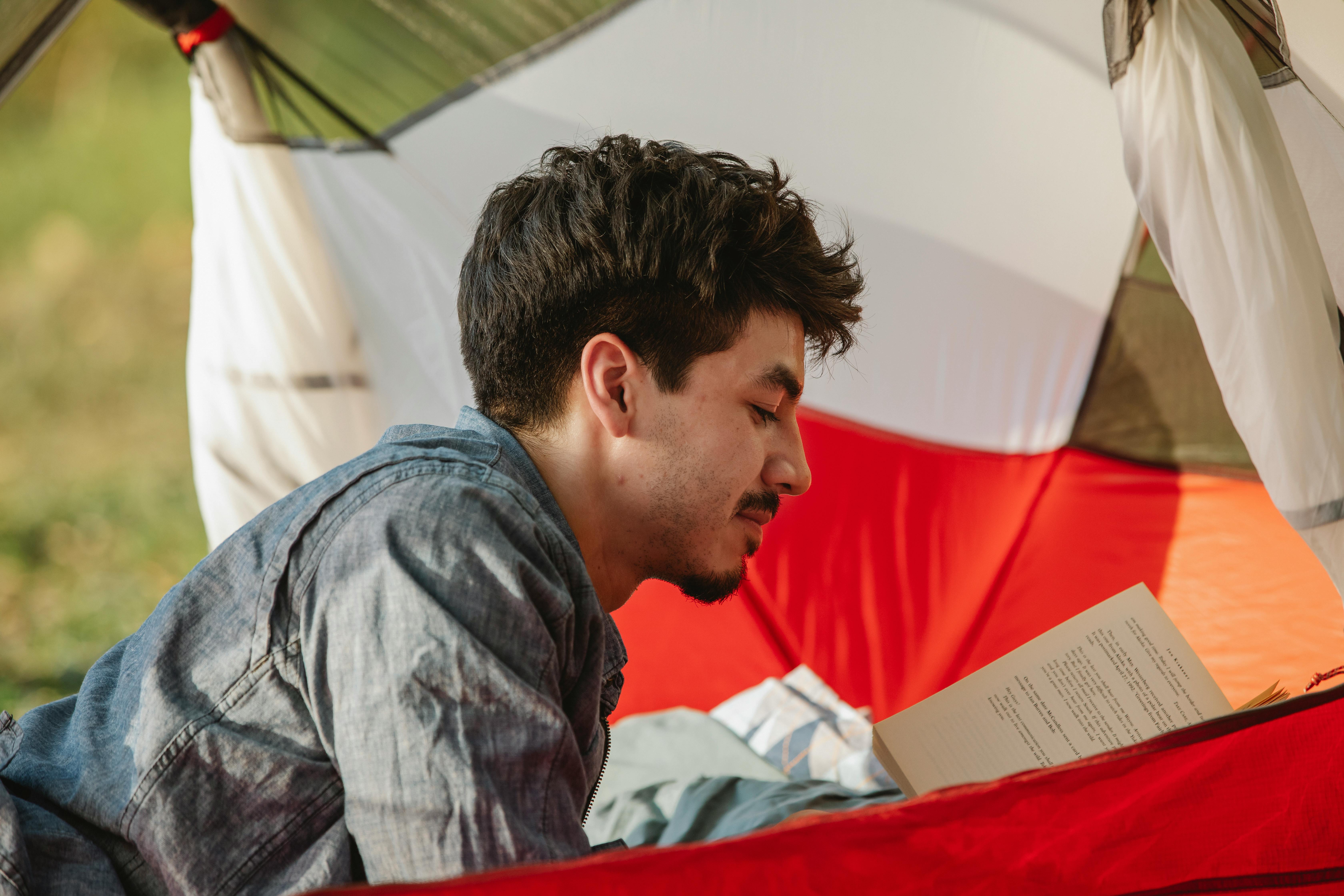 traveler reading textbook in tent during summer journey