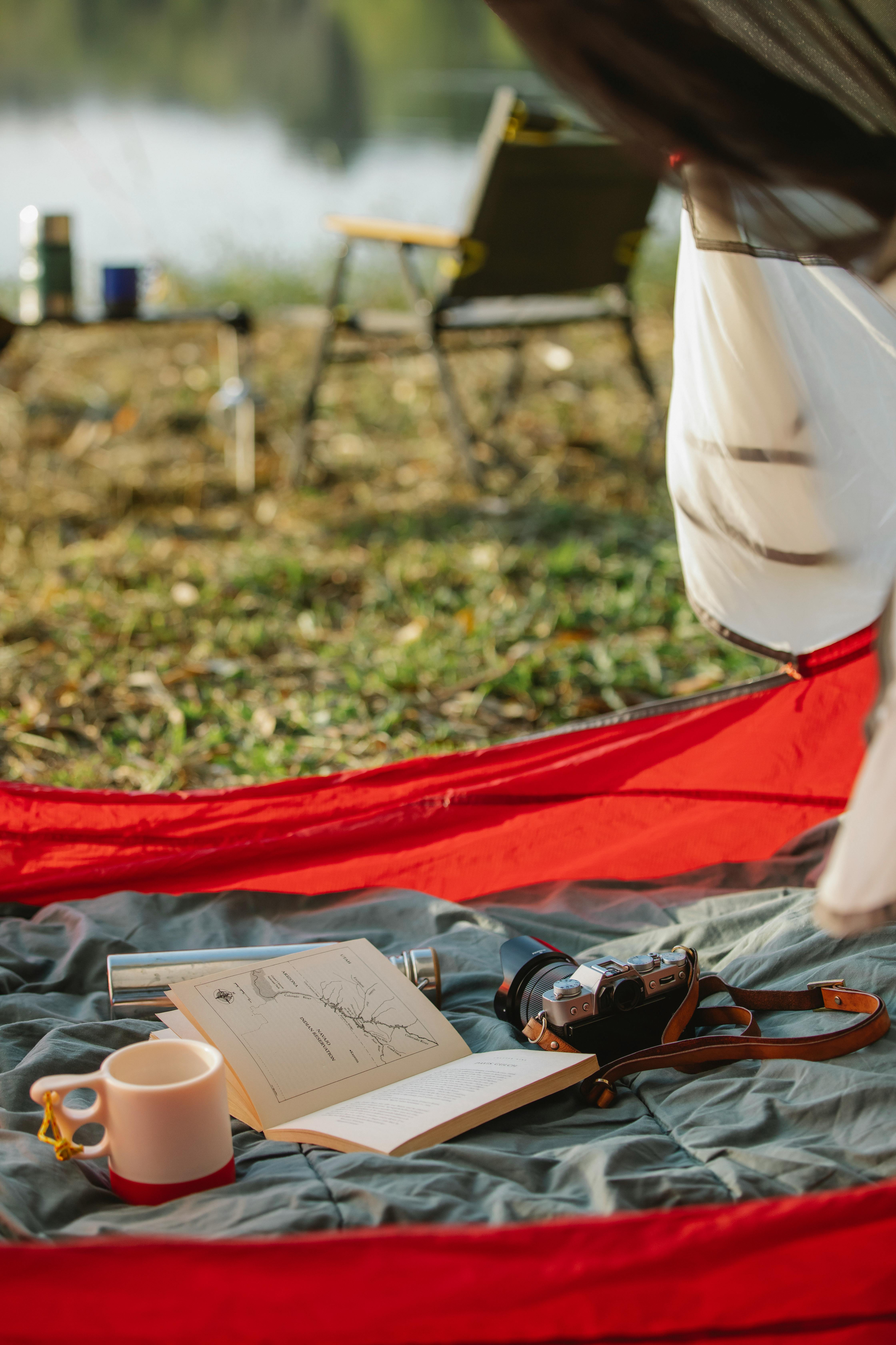 book with mug and photo camera in tent against river