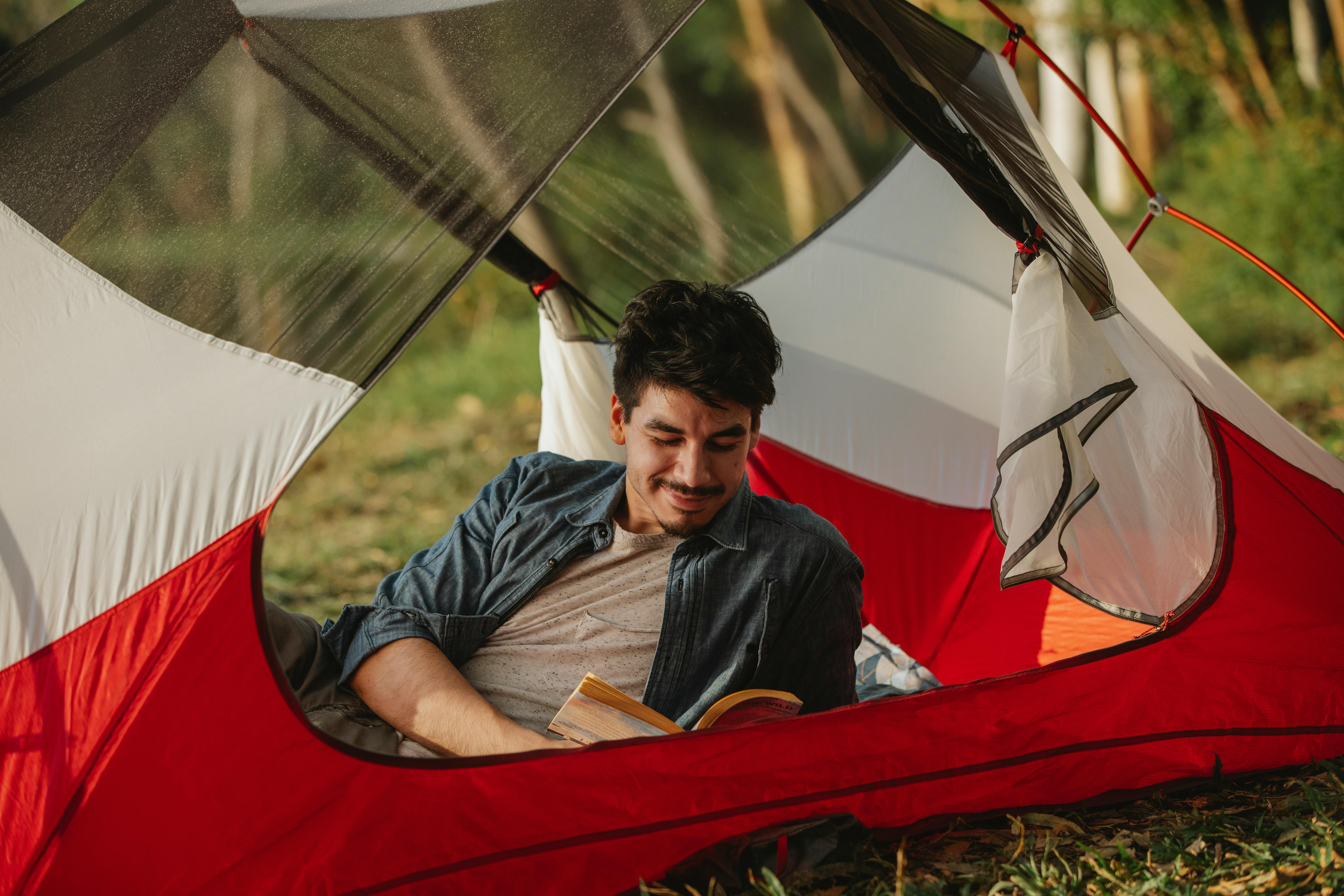 smiling young guy reading novel in tent