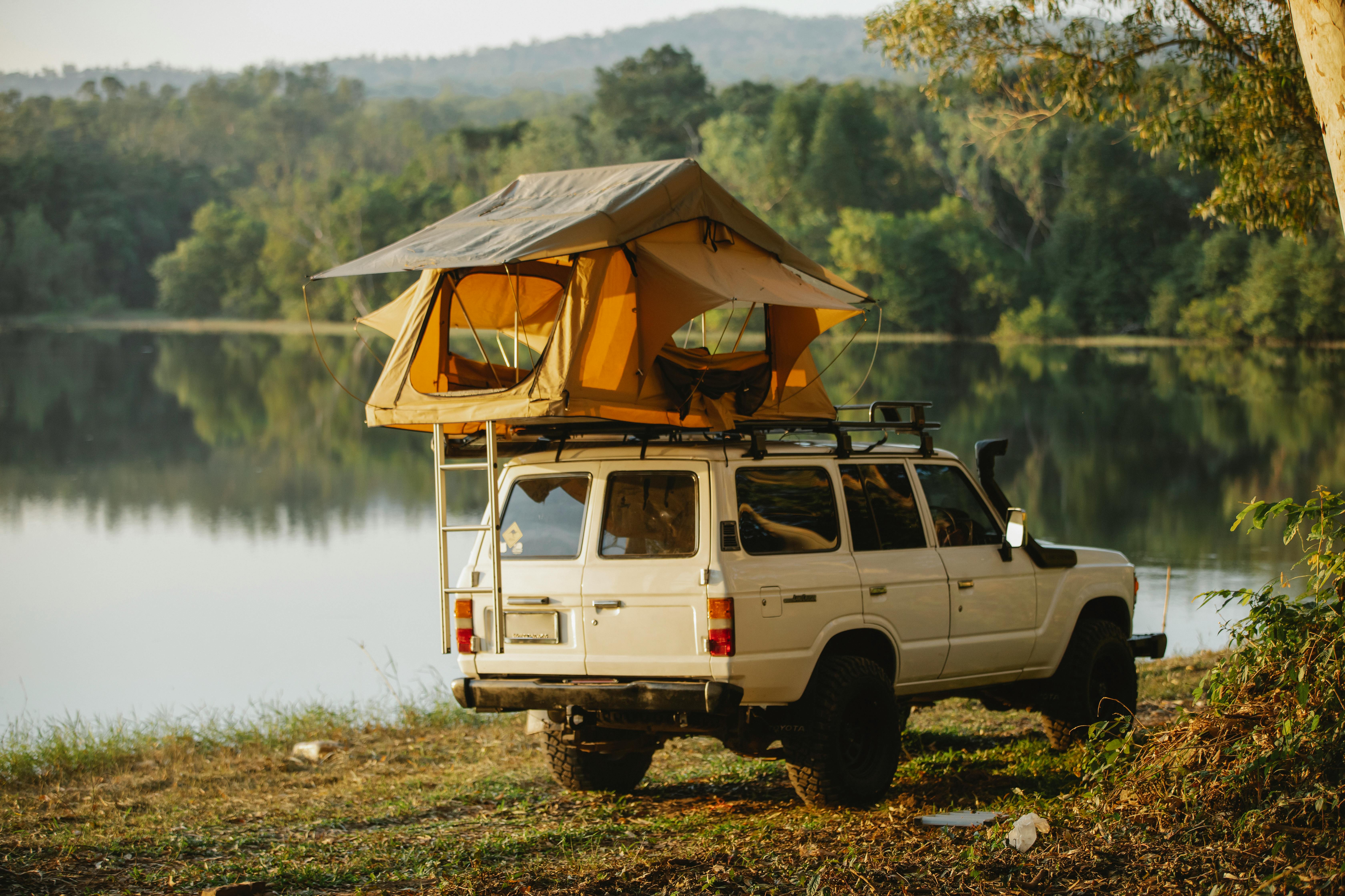 off road car with tent on roof parked on lake shore in forest