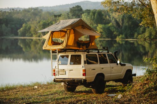Free Off road car with tent on roof parked on lake shore in forest Stock Photo