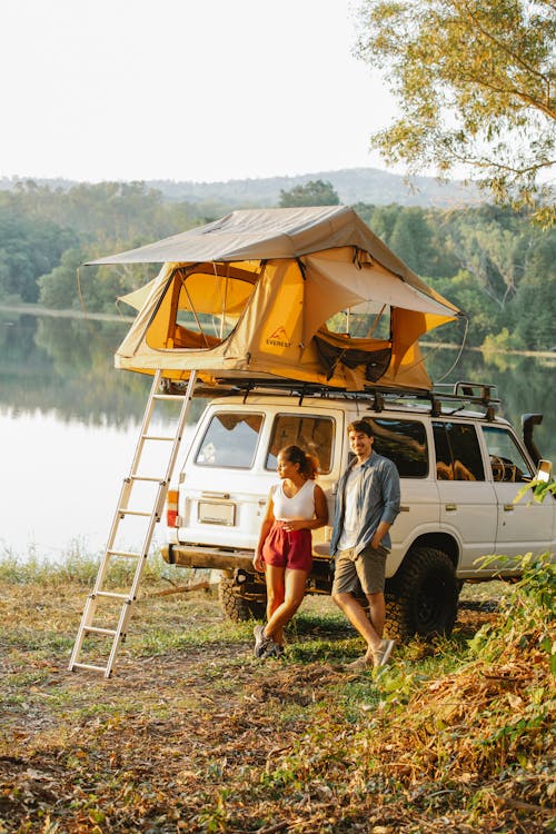 Multiracial couple relaxing at lakeside near tent placed on car roof during road trip