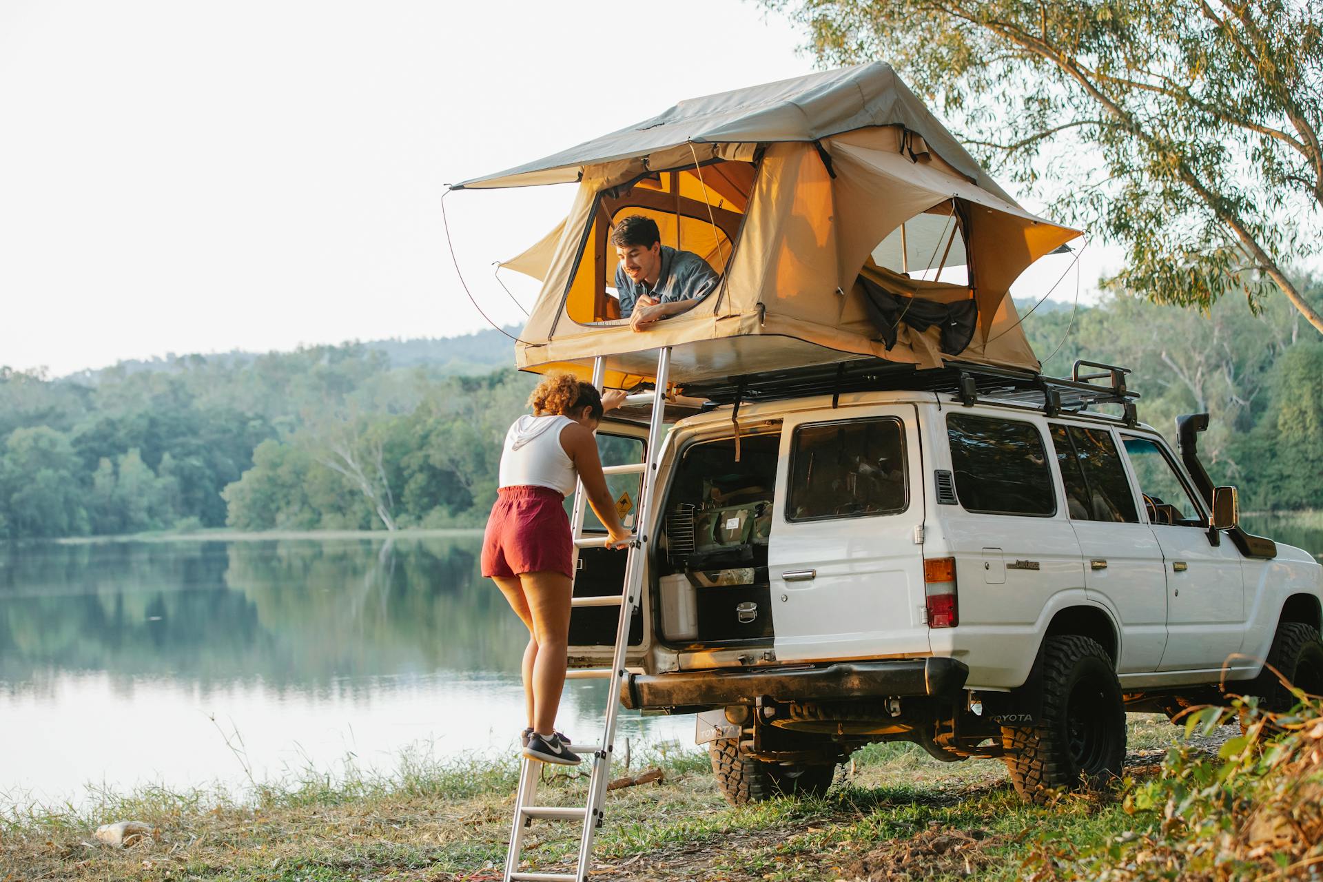 Unrecognizable woman standing on ladder near boyfriend recreating in tent during camping at lakeside