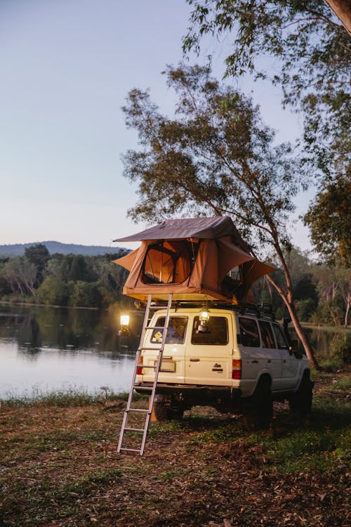 Camping tent on top of off road vehicle parked near lake in evening