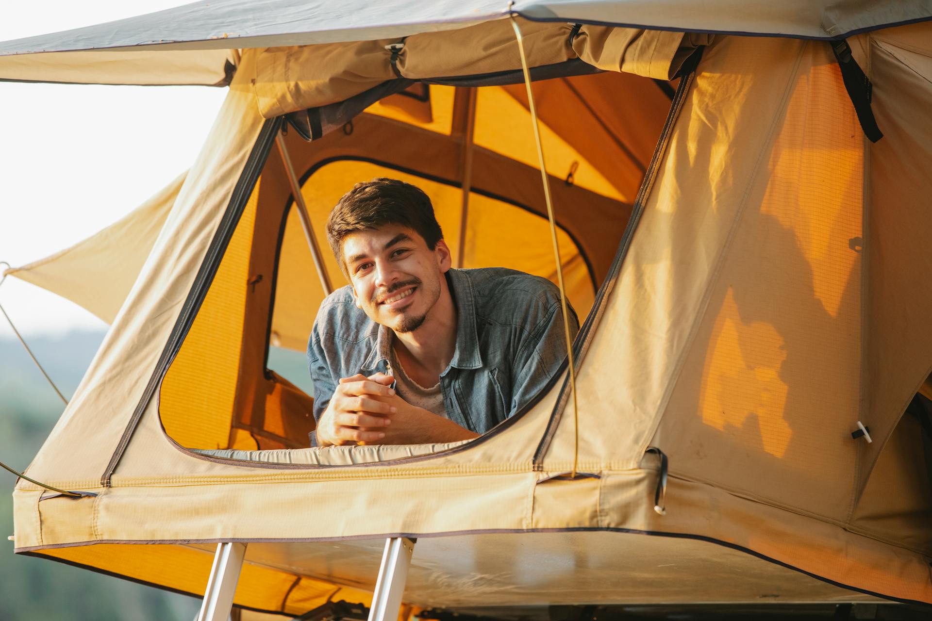A cheerful young man smiling from inside his camping tent during a sunny outdoor expedition.
