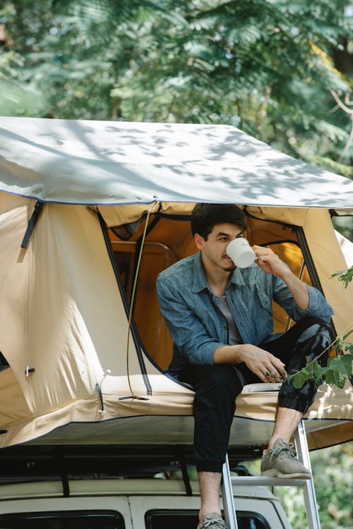 Free Young man drinking coffee in tent during camping in forest Stock Photo