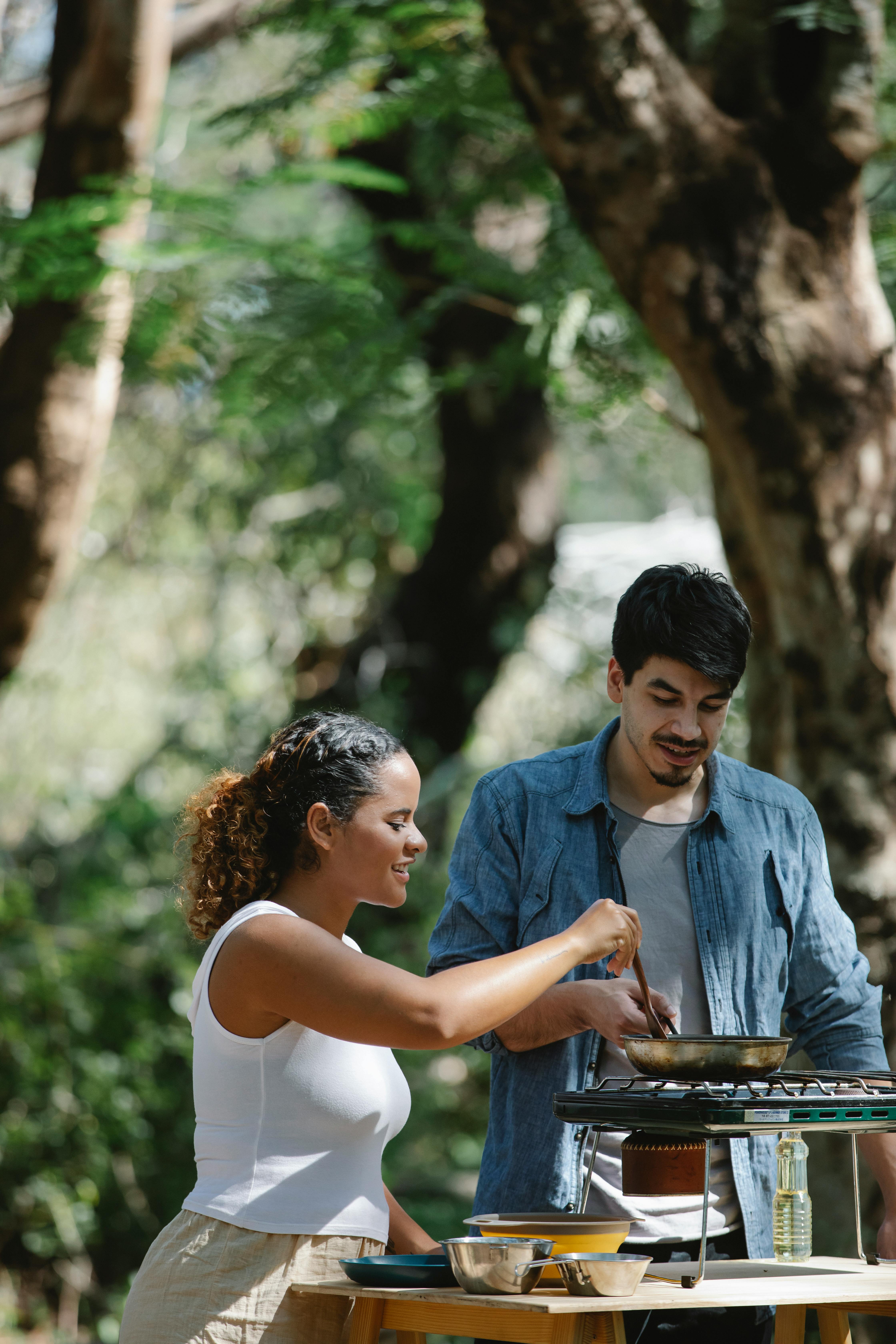Happy couple cooking together outdoors on a sunny day, enjoying nature and bonding.