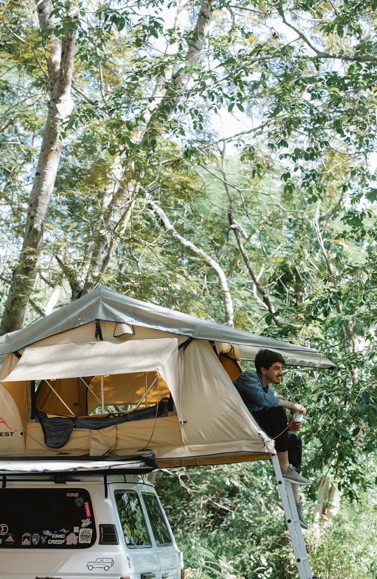 Smiling Young Man Resting In Camp Tent Placed On Car Parked In Forest