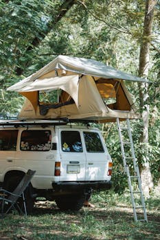 A white SUV with a roof tent set up in a lush forest camping site, ideal for adventures.