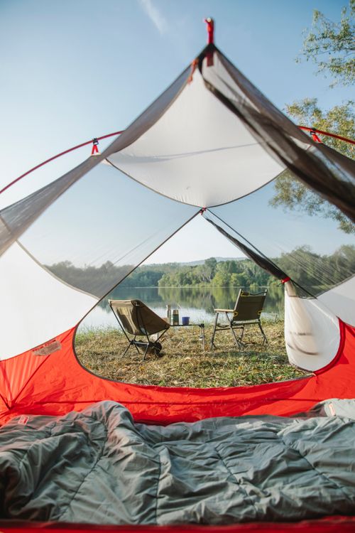 Free View thought empty camping tent on grassy coast with chairs placed near calm river in countryside in sunny day Stock Photo