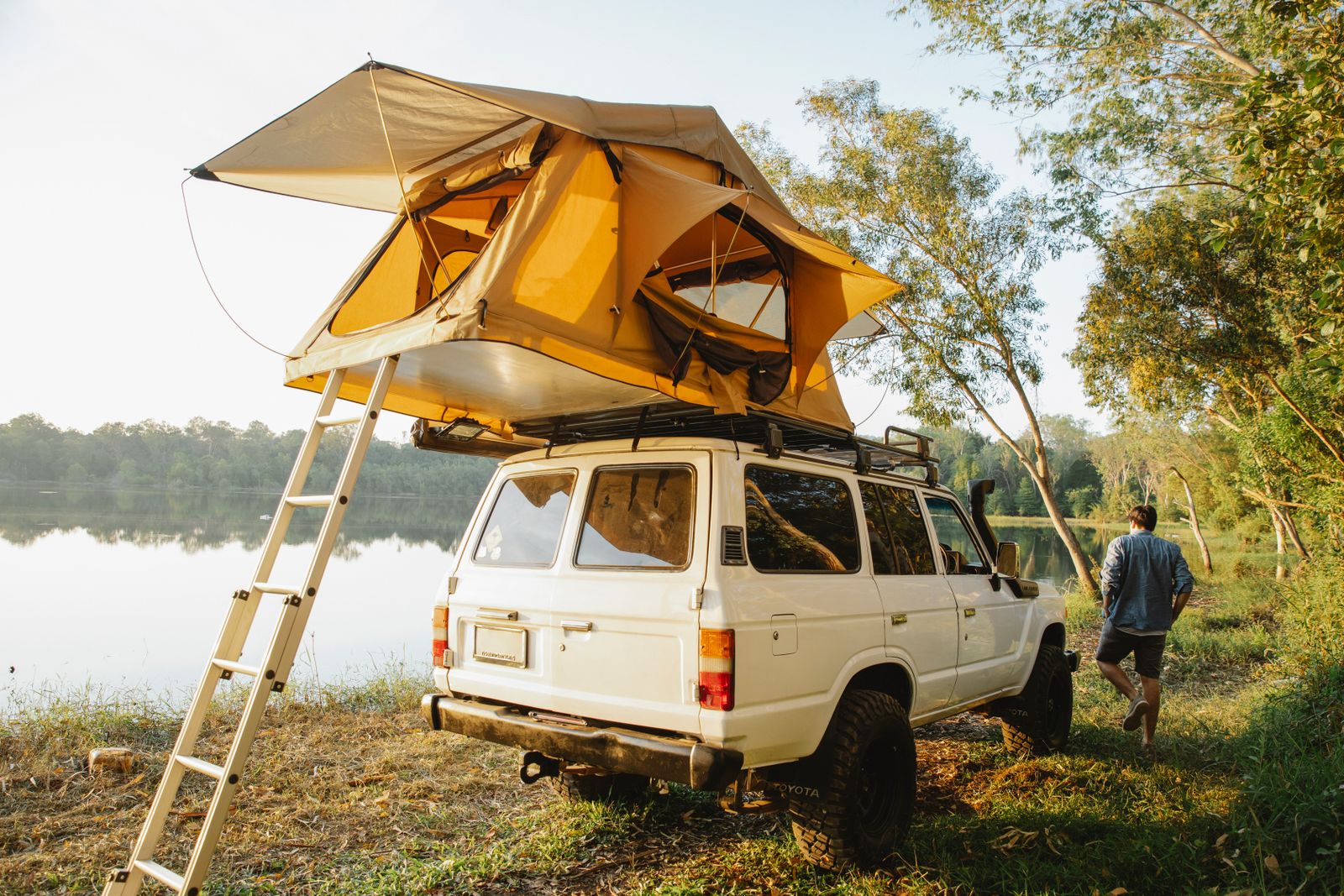 Person setting up a roof top tent on a vehicle by a lake