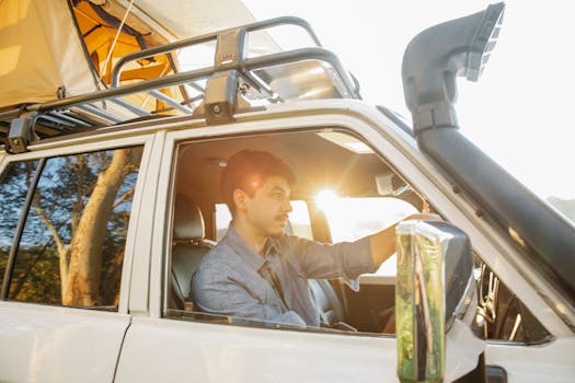 Side view of unshaven man driving car with tent on roof and looking away while having weekend trip on sunny weather