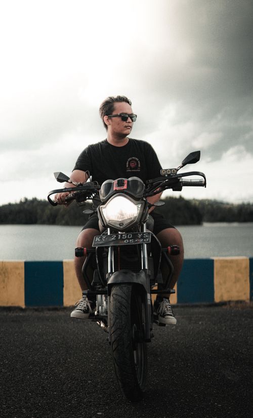 Free A man wearing sunglasses rides a motorcycle by a lakeside road. Stock Photo