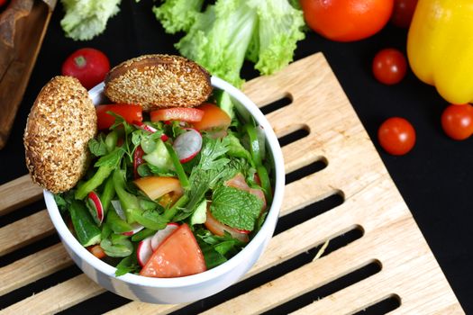 Vibrant bowl of fresh vegetable salad with sesame bread, ideal for healthy eating concepts.