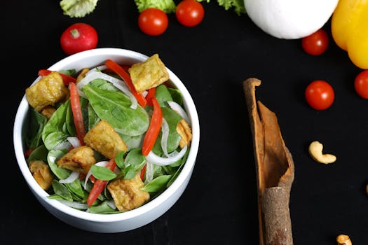 Colorful vegetable salad with crispy tofu, spinach, and fresh ingredients on black background.