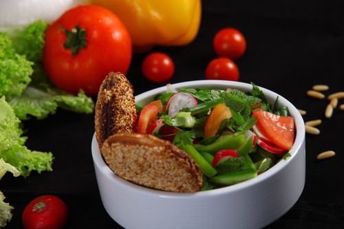 Free A colorful vegetable salad with crackers and fresh greens, beautifully presented on a black background. Stock Photo
