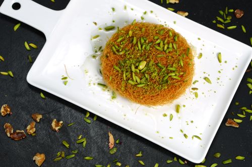 Free Close-up of knafeh dessert topped with green pistachios on a white plate, over a black background. Stock Photo