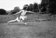 A Grayscale Photo of a Woman Doing a Lunge while Holding a Javelin