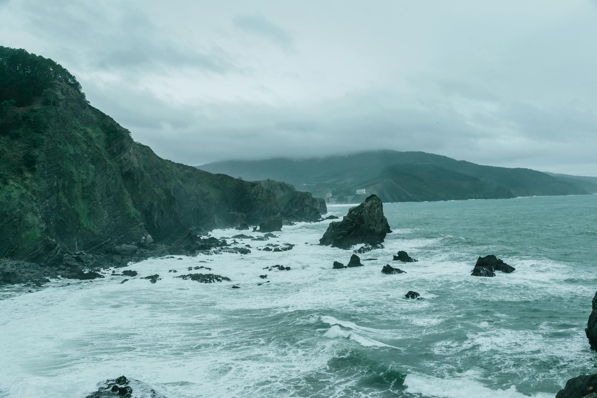 Picturesque scenery of stormy ocean with foamy waves crashing over rocky cliffs against dramatic foggy sky in Gaztelugatxe island located in Basque Country