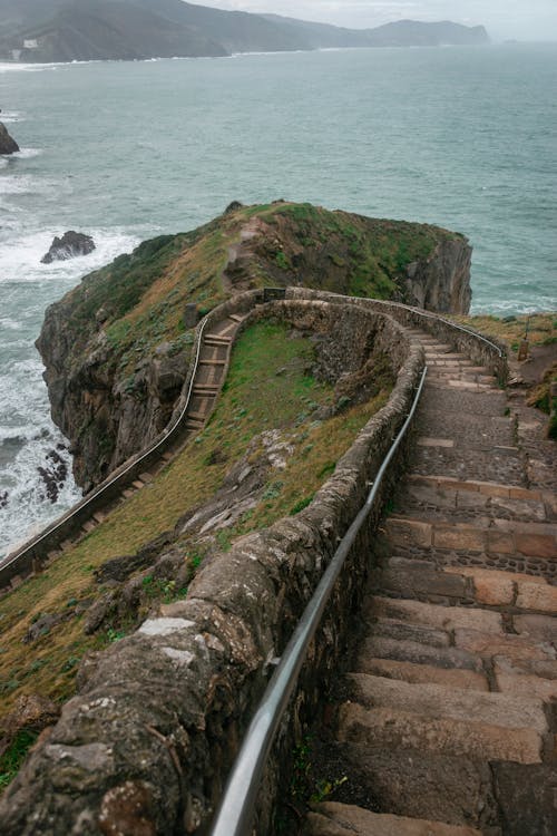 From above of curvy stone staircase leading down from San Juan de Gaztelugatxe church located on rocky island in stormy sea on cloudy day