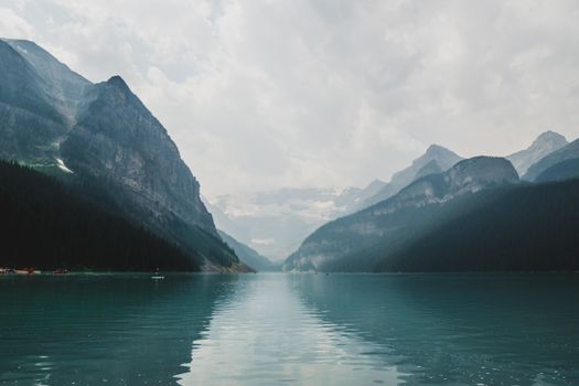 Majestic peaceful lake reflecting high stony mountains under sky with gray cumulus clouds